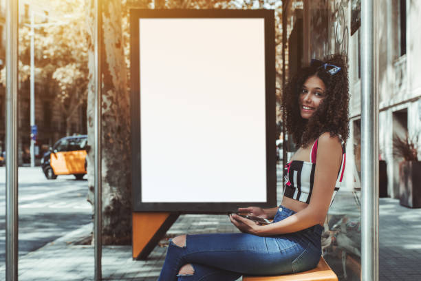 istock Curly woman on bus stop with empty billboard template behind 1037027458