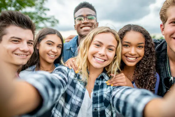 A diverse group of students take a selfie outside. They look silly and happy to be together.