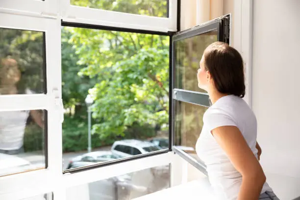 Side View Of A Woman Looking Through Window At Home