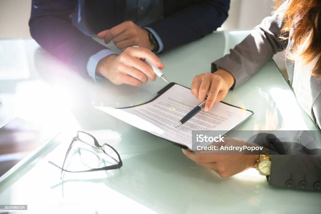 Two Businesspeople Analyzing Document Two Businesspeople Hand Analyzing Document Over Glass Desk Contract Stock Photo
