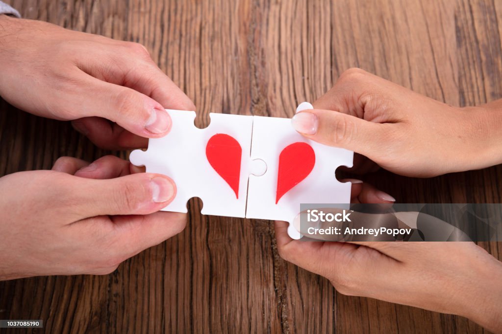 Couple Connecting Red Heart Puzzle Together Elevated View Of A Couple Connecting Red Heart Puzzle Together On Wooden Desk Above Stock Photo