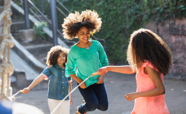 African-American sisters jumping rope Three African-American sisters having fun playing on a playground with a jump rope. The one in the middle jumping in mid-air is 12 years old. Her sisters are 11 and 13. jump rope stock pictures, royalty-free photos & images