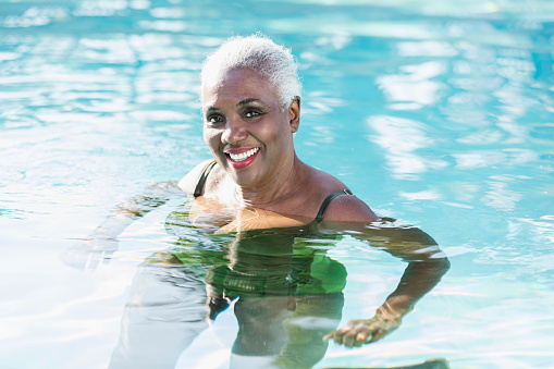 A senior African-American woman in her 60s in a swimming pool, smiling and looking at the camera.