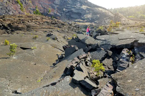 Young female tourist exploring surface of the Kilauea Iki volcano crater with crumbling lava rock in Volcanoes National Park in Big Island of Hawaii, USA