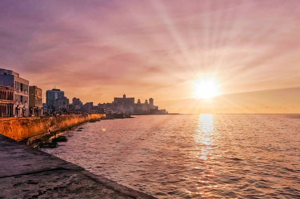 Sunset over Malecon and Atlantic Ocean with residential building and visible sun rays - Havana, Cuba