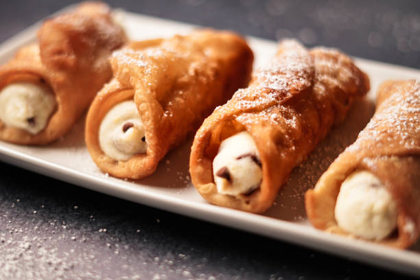 Stuffed Fresh Cannoli Feshly made cannoli. Crispy shells are filled woth luscious ricotta and marscapone cheese with a hint of lemon zest and mini chocolate chips. Served on a white platter with dusted powedered sugar. cannoli photos stock pictures, royalty-free photos & images
