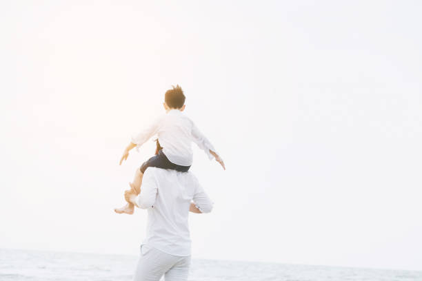 Photo of a father and his son, enjoying their bonding day at the beach by the wavy ocean