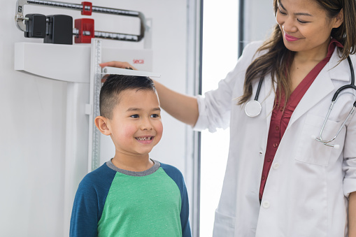 A cute young boy stands on the scale at the doctor's office while the female doctor measures his height.