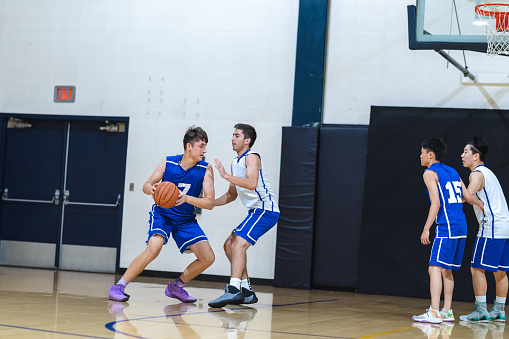 A high school player dribbles and tries to get around his opponent, who is guarding him closely, during a game. He's about to put a shot up. Two other players are jockeying for position under the basket.