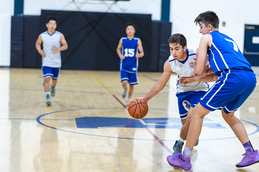A high school player dribbles and tries to get around his opponent, who is guarding him closely, during a game.