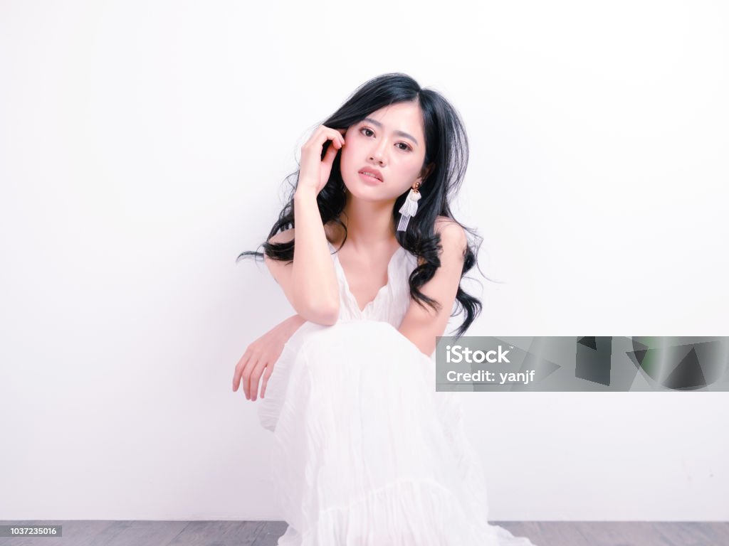 Beautiful Chinese Girl Sit On Floor With Hand On Face Against White Wall  Background Portrait Of Romantic Young Female Looking At Camera With Sexy  Expression Stock Photo - Download Image Now - iStock
