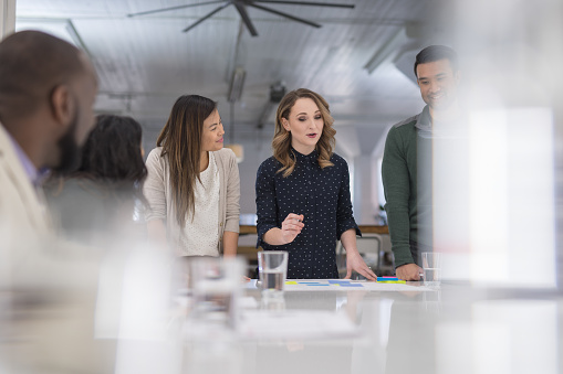 The CEO of a business startup gathers her multiethnic team around the conference table to finalize a product launch. She is signing paperwork and her coworkers are watching next to her.