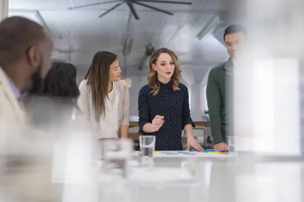 The CEO of a business startup gathers her multiethnic team around the conference table to finalize a product launch. She is signing paperwork and her coworkers are watching next to her.