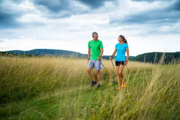 active smiling middle aged couple doing nordic walking sport in grassland with  shallow focus cloudy overcast sky dark clouds front view