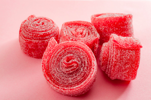 Chewy sweets and strawberry and cherry flavoured gummy candy concept with close up on sweet and sour red sour belts covered in sugar isolated on a pink background