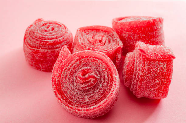 Closeup  on gummy sweet treats isolated on pink background Chewy sweets and strawberry and cherry flavoured gummy candy concept with close up on sweet and sour red sour belts covered in sugar isolated on a pink background rolling stock pictures, royalty-free photos & images