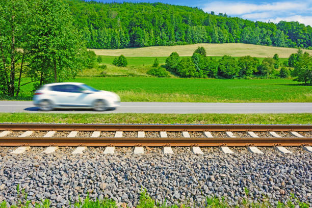 A fast moving car along the road goes alongside the railway tracks. Tracks running next to the road. A sunny view of a car passing through the countryside