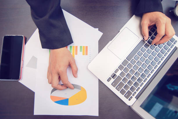 istock hand holding graph sheet and pressing laptop 1037372180