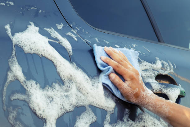 istock Woman's hand with blue sponge in soapy foam washes car 1037378710