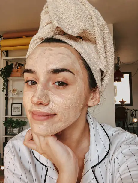 Young woman taking a selfie and creating a DIY facial mask tutorial