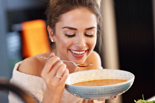 Adult woman eating pumpkin soup in the kitchen Picture of adult woman tasting pumpkin soup in the kitchen soup stock pictures, royalty-free photos & images