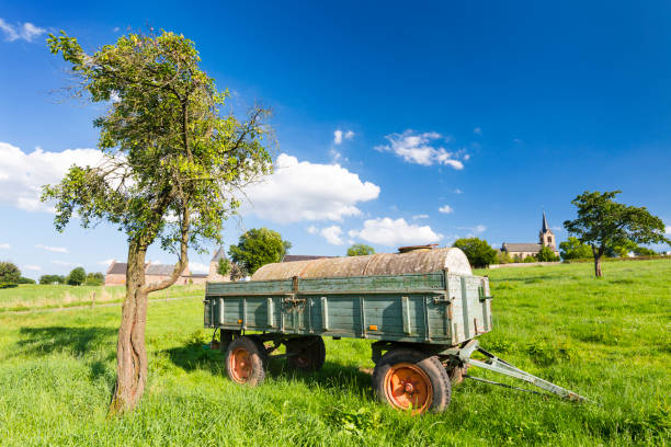 An old fertilizer trailer on a green meadow with a village in the background and blue sky.