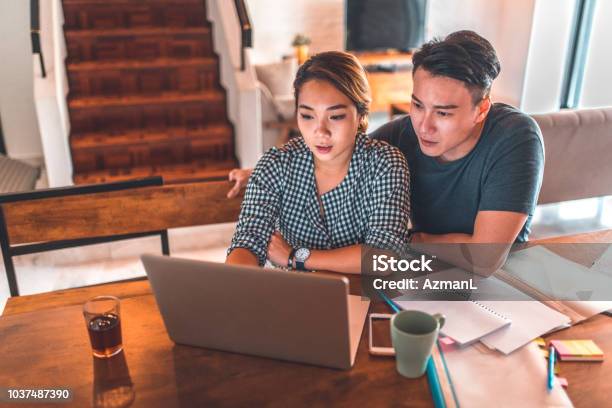 Serious Couple Using Laptop While Sitting At Home Stock Photo - Download Image Now - Couple - Relationship, Looking, Laptop