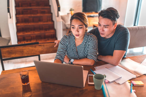 serious couple using laptop while sitting at home - paper document notebook laptop imagens e fotografias de stock