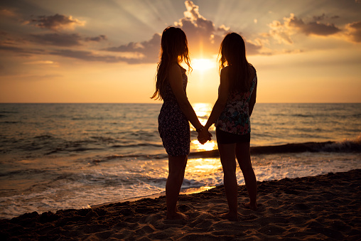 Two women on the beach in Italy / Tuscany at sunset hold each other's hands.