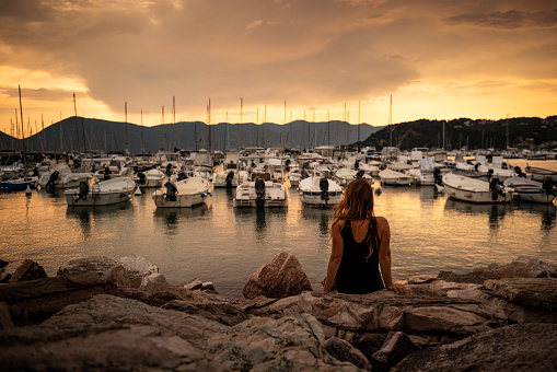 Young woman in an Italian harbor with boats in the background at sunset.