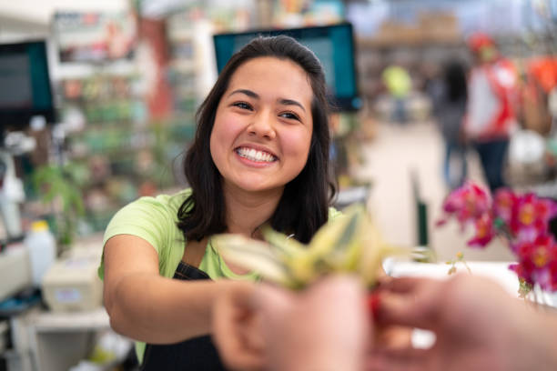 porträt von zuversichtlich mitarbeiter kasse geben eine blume am blumenmarkt - supermarket sales clerk retail cashier stock-fotos und bilder