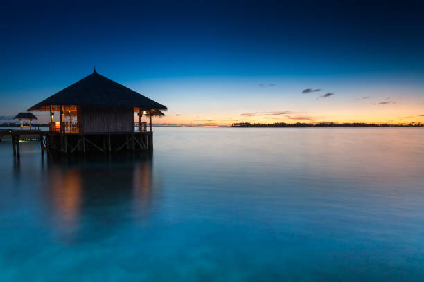 Maldivian Tropical Sunset with Bamboo Villa and Lights on smooth Ocean