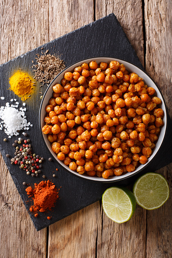 Snack of fried chickpeas with spices close-up in a bowl on the table. Vertical top view from above