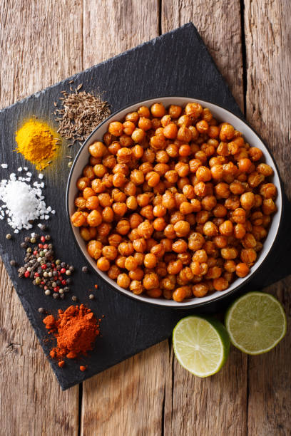 Snack of fried chickpeas with spices close-up in a bowl. Vertical top view Snack of fried chickpeas with spices close-up in a bowl on the table. Vertical top view from above chick pea stock pictures, royalty-free photos & images