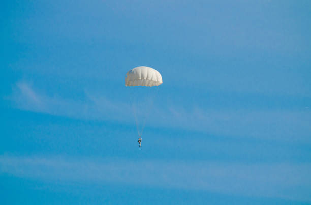 The parachutist flying in a blue sky on a white dome parachute