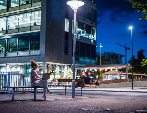 Businesswoman using laptop outdoors in the city at night. stock photo