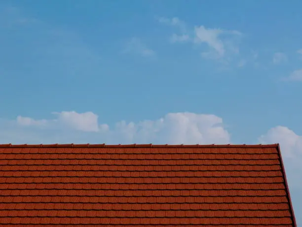 red clay tile roof abstract with blue sky and white clouds above