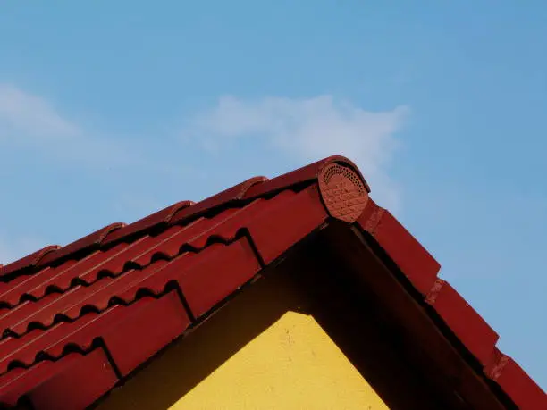 red clay tile roof abstract with yellow wall and blue sky and white clouds above