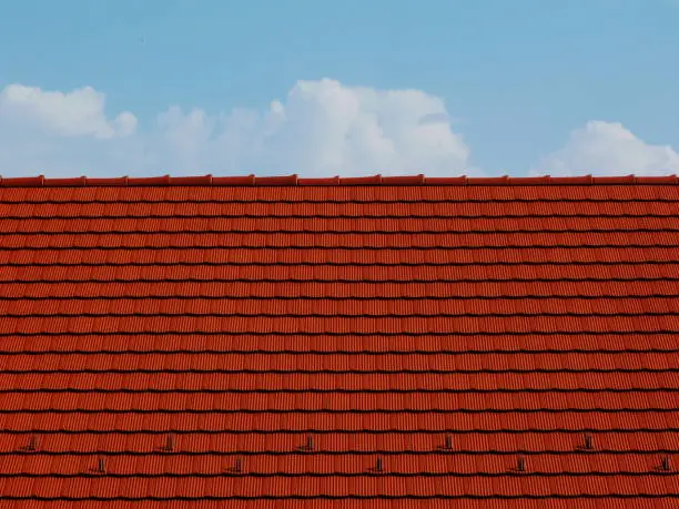 red clay tile roof abstract with blue sky and white clouds above