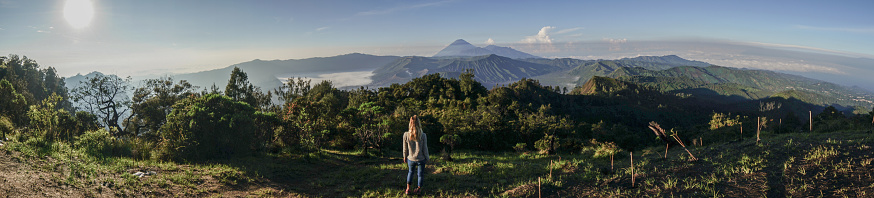 Young woman hiking contemplates volcanic landscape from top of hill looking at Bromo volcanoes- People travel adventure concept