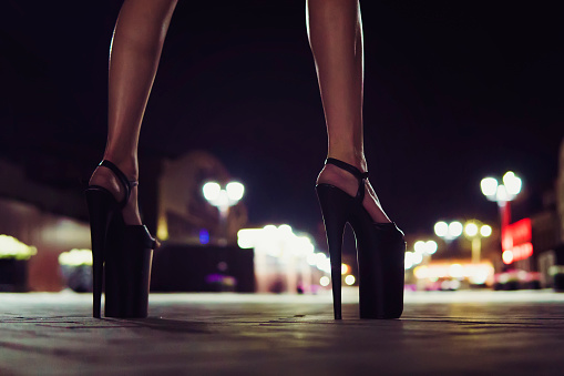 High-heeled shoes for performing on stage for Striptease. Beautiful elegant sexy female legs close up on the night street of the city on the background of glowing lanterns.