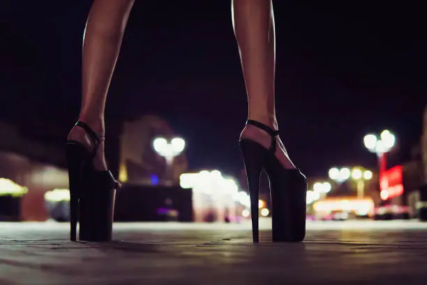 High-heeled shoes for performing on stage for Striptease. Beautiful elegant sexy female legs close up on the night street of the city on the background of glowing lanterns.