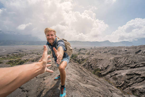 junger mann wandern, zieht hand eines teamkollegen zu erreichen. eine helfende hand an die spitze der vulkan krater erreichen. bromo vulkan region in indonesien, asien - bromo crater stock-fotos und bilder