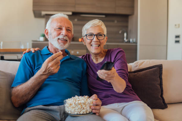 Senior couple watching TV Elderly couple eating popcorn and watching TV together watching tv stock pictures, royalty-free photos & images