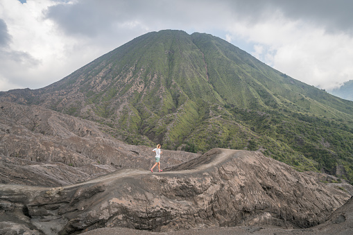 Young woman running on cross country dirt trail in Indonesia on volcanoes with dramatic landscape. People travel adventure fun concept