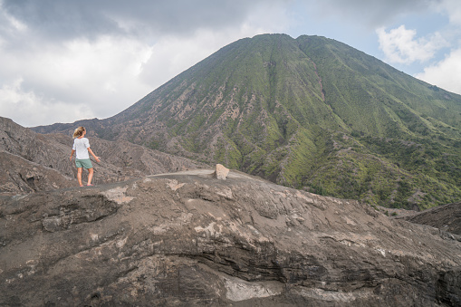 Young woman hiking stands arms outstretched on top of mountain with Bromo volcanoes view in Indonesia- People travel fun adventure concept success and achievement