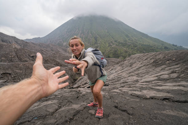 молодая женщина походы, вытаскивает руку, чтобы достичь одного из товарища по команде. рука помощи, чтобы достичь вершины вулкана кратера. в - bromo crater стоковые фото и изображения