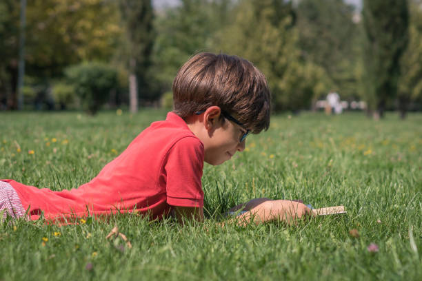 istock Schoolboy reading book on the grass 1037648520