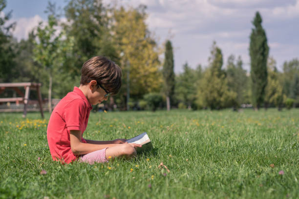 istock Schoolboy reading book on the grass 1037650388