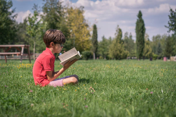 istock Schoolboy reading book on the grass 1037650498